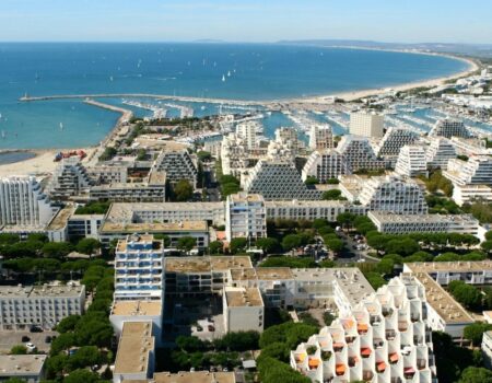 Aerial view of La Grande-Motte, the French coastal city designed by Jean Balladur, showing its pyramid-shaped buildings, marina and extensive green landscape.