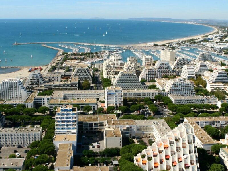 Aerial view of La Grande-Motte, the French coastal city designed by Jean Balladur, showing its pyramid-shaped buildings, marina and extensive green landscape.