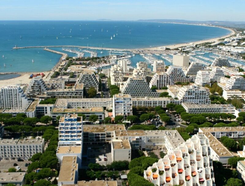 Aerial view of La Grande-Motte, the French coastal city designed by Jean Balladur, showing its pyramid-shaped buildings, marina and extensive green landscape.
