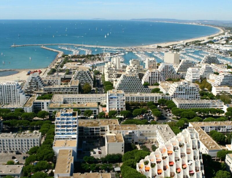 Aerial view of La Grande-Motte, the French coastal city designed by Jean Balladur, showing its pyramid-shaped buildings, marina and extensive green landscape.