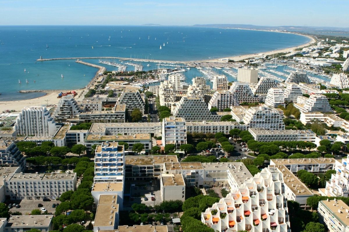Aerial view of La Grande-Motte, the French coastal city designed by Jean Balladur, showing its pyramid-shaped buildings, marina and extensive green landscape.